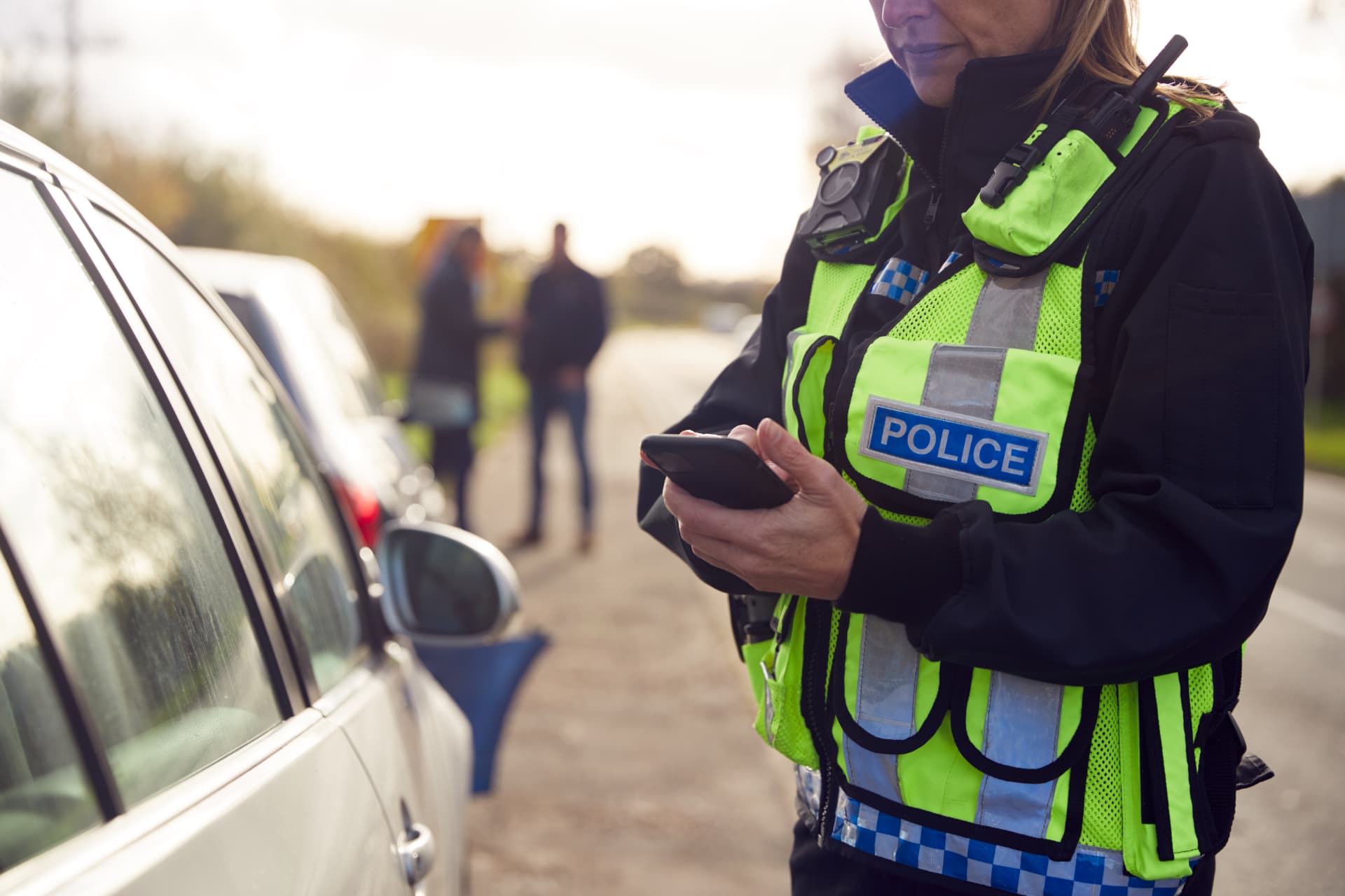 A police officer using a mobile phone beside a car.