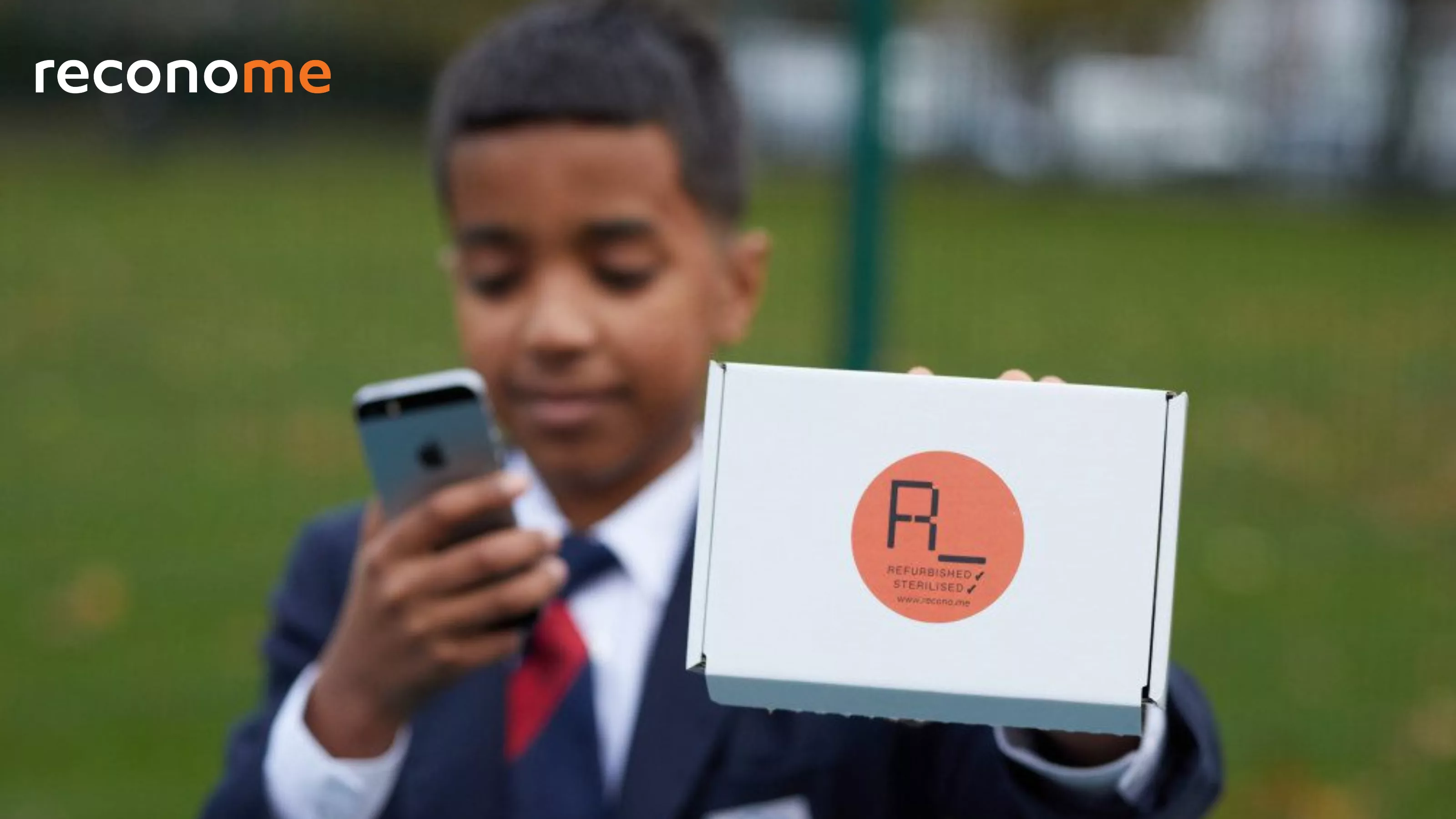A young person holding a phone beside a laptop box.