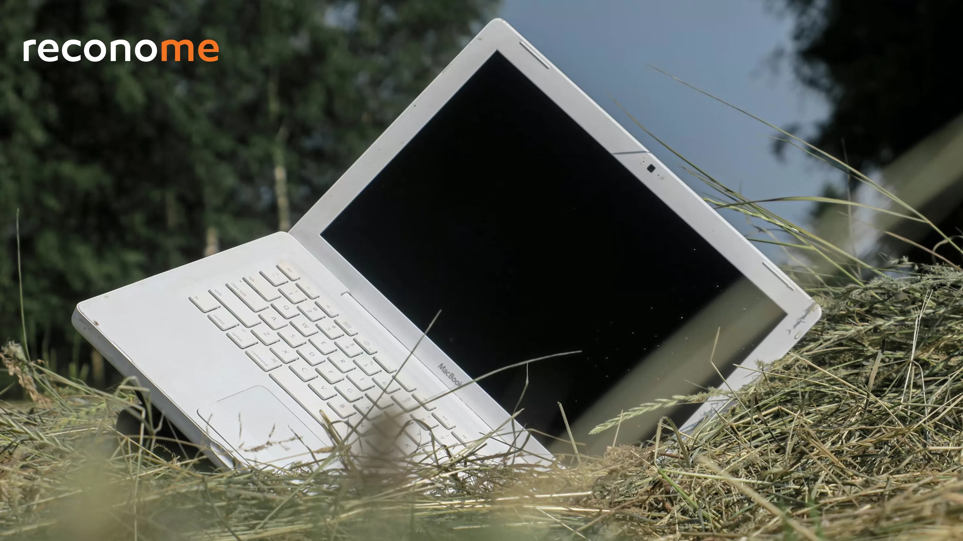 A discarded laptop lying in long grass.