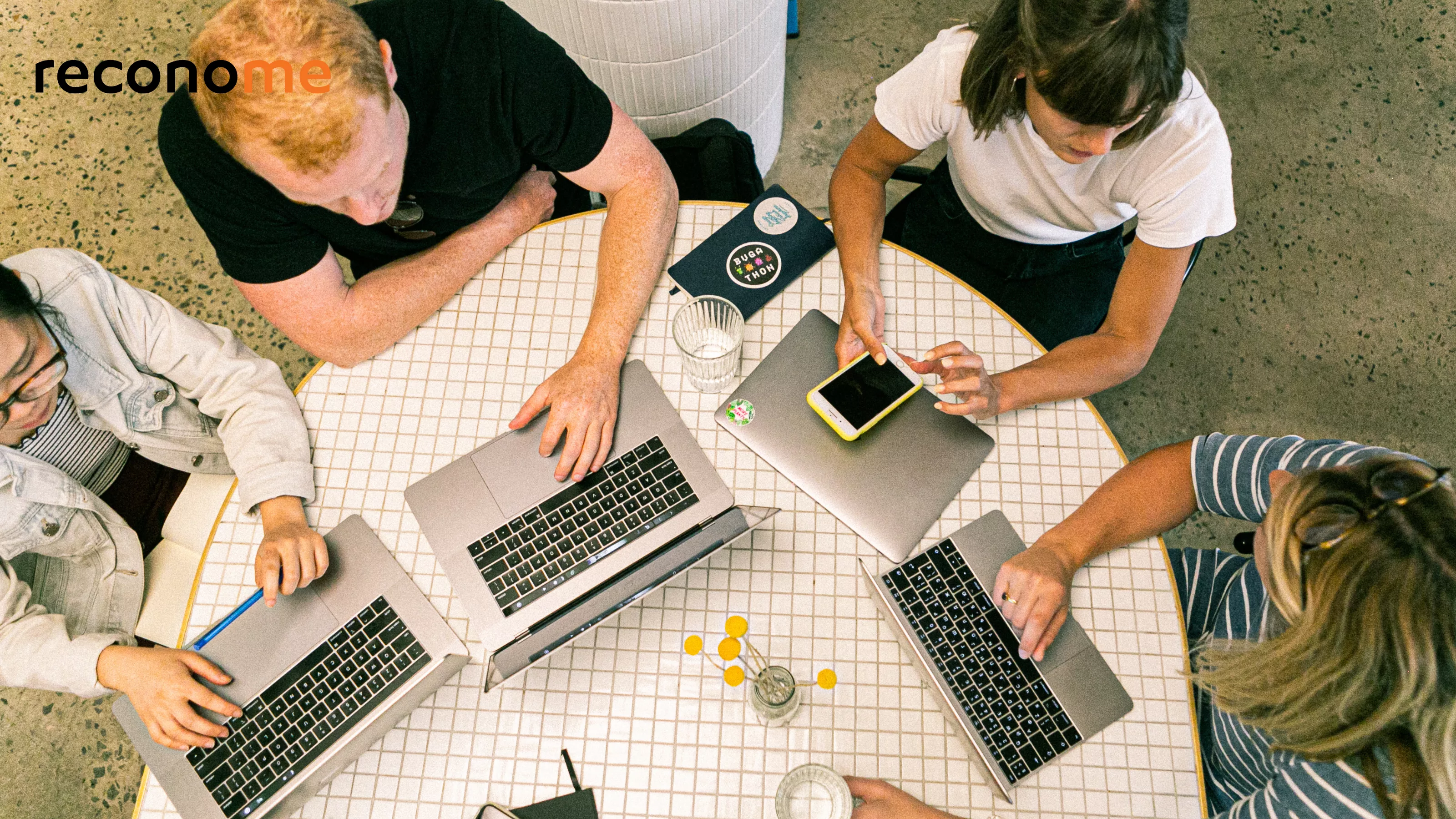 People around a desk with laptops and notepads.